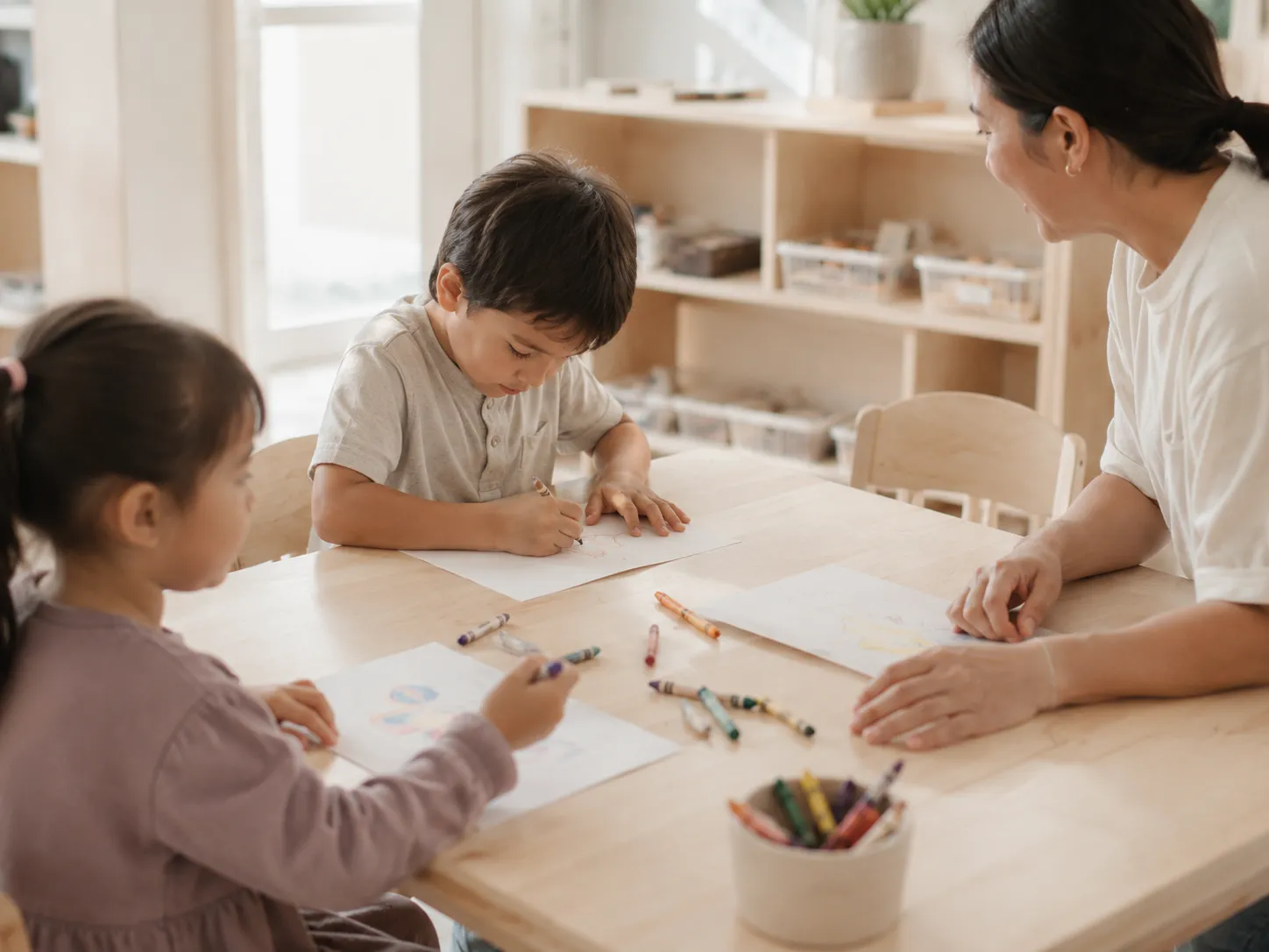 Children drawing with an educator at a classroom table